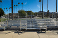 Metal bleachers on a concrete surface with palm trees and mountains in the background.