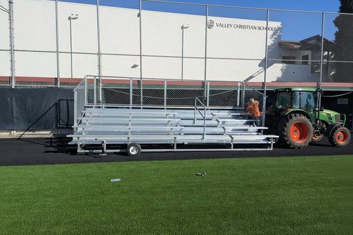 Metal bleachers on a trailer with people in safety vests near a school building.